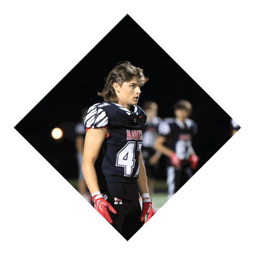 A person wearing a black football uniform with the number 41 and red gloves stands on a field at night with other players in the background. Description generated by AI