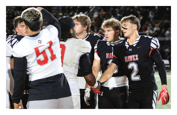 People wearing football uniforms from two different teams are shaking hands on a field after a game. Description generated by AI