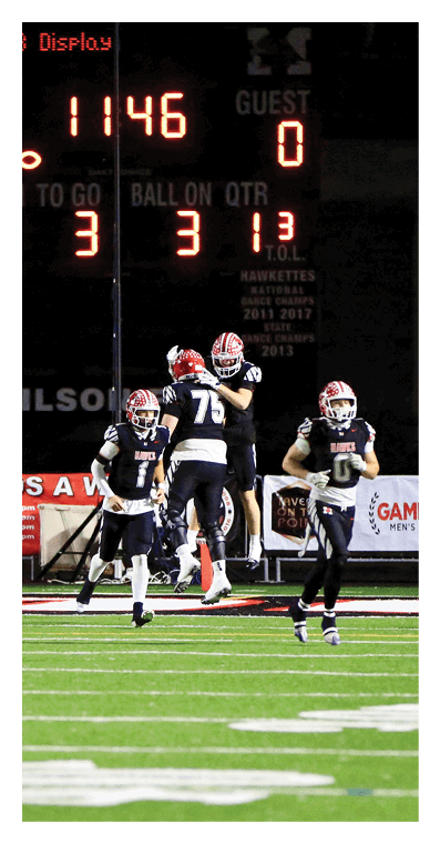 A scoreboard displays the numbers 46 and 31 with the words “BALL ON QTR" visible above three people wearing football helmets and uniforms. Description generated by AI