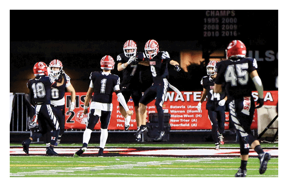 People in football uniforms are celebrating on a field under a scoreboard showing a score of 34. Description generated by AI