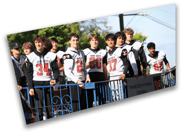 A group of people wearing matching sports jerseys stand behind a blue railing outdoors on a sunny day. Description generated by AI