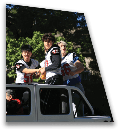 Three people wearing football jerseys are standing in the back of a white vehicle while one person is seated inside the vehicle. Description generated by AI