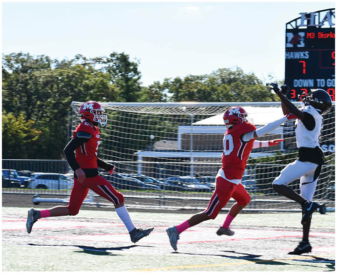 Three people in football uniforms are actively playing on a field with one person in white jumping to catch a ball while two others in red chase behind. Description generated by AI