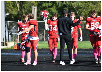 A group of people in red football uniforms with pink socks are standing and interacting on a track field near a chain-link fence. Description generated by AI