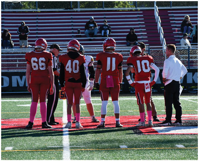 Several people in football uniforms and officials stand on a field near the center with empty bleachers in the background. Description generated by AI