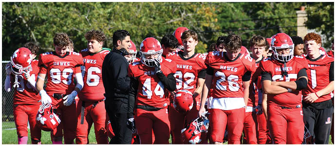 A group of people wearing red football uniforms with helmets stand together outdoors on a grassy field. Description generated by AI