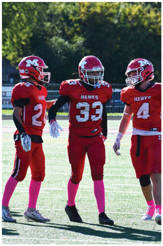 Three people wearing red football uniforms with pink socks stand on a field engaged in conversation or planning. Description generated by AI