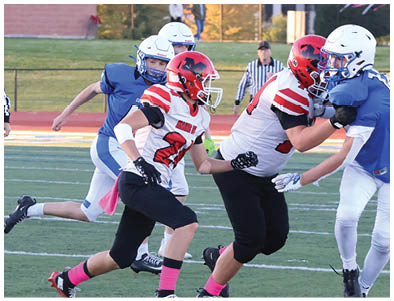 Several people wearing football helmets and uniforms are actively playing on a grassy field with referees observing in the background. Description generated by AI