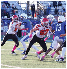 People wearing football uniforms and pink socks are playing on a grassy field with bleachers and a few spectators in the background. Description generated by AI
