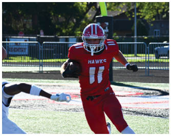 A person in a red football uniform with the word “HAWKS" is running on a field while holding a football and evading a person in a white uniform reaching out to tackle them. Description generated by AI