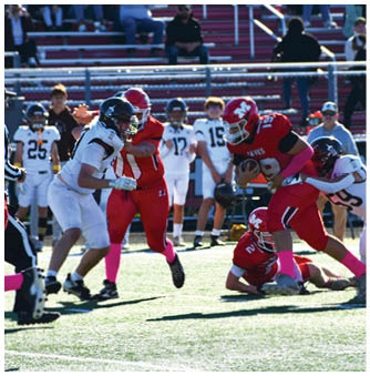 A group of people in football uniforms are actively playing on a sunlit field with some players tackling and others running. Description generated by AI