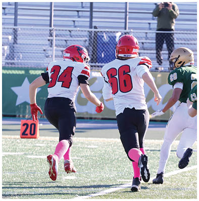 Two people wearing football uniforms with red helmets and pink socks are running on a field near a marker showing the number 20. Description generated by AI