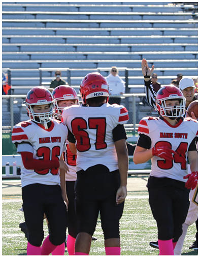 Four people in red and white football uniforms stand on a field with one raising an arm, and a referee in the background also raising an arm. Description generated by AI