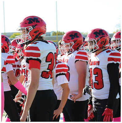 A group of people wearing red helmets and white football jerseys with red and black details are standing together on a field. Description generated by AI