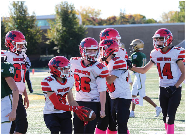 Several people wearing red and white football uniforms with helmets are gathered on a field, with one person holding a football. Description generated by AI