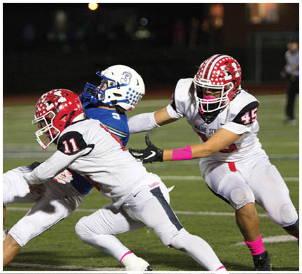 Three people in football uniforms and helmets are engaged in a play on a field, with two players in white and red uniforms tackling a player in a blue and white uniform. Description generated by AI