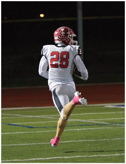 A person wearing a white football uniform with the number 28 and a red helmet is running on a football field at night. Description generated by AI