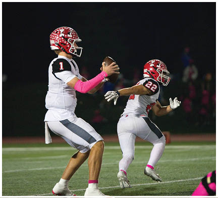 Three people wearing football uniforms and pink accessories are running on a field during a game. Description generated by AI