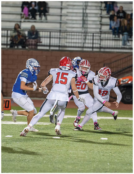 Several people wearing football uniforms are actively engaged in a play on a field with spectators in the background. Description generated by AI