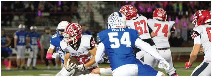 A person in a white and red football uniform is running with the ball while being pursued by players in blue and white uniforms on a football field. Description generated by AI