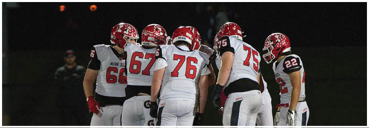 A group of football players in red and white uniforms are huddled together on a field at night. Description generated by AI