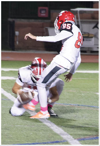 Two people in sports uniforms are engaged in a football play on a field with one person crouching and the other mid-air. Description generated by AI