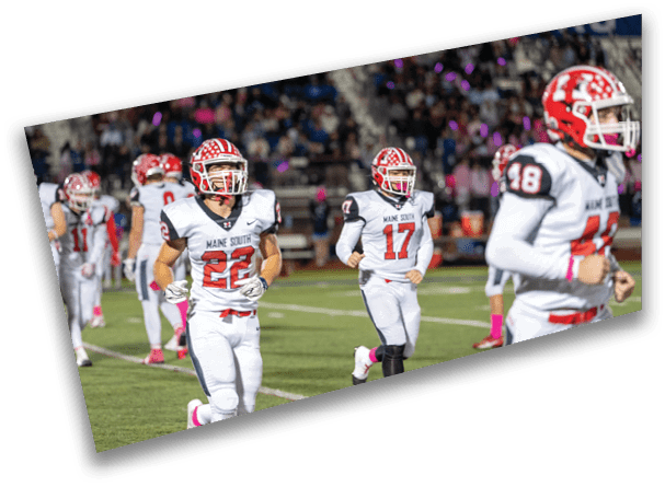 People in football uniforms with red and white helmets are walking on a field with a crowd in the background. Description generated by AI