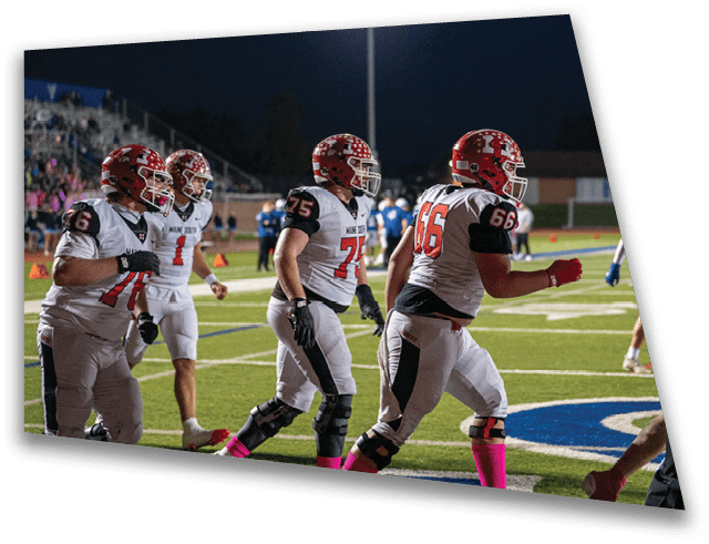 Several adults wearing football uniforms and helmets are walking on a well-lit football field at night. Description generated by AI