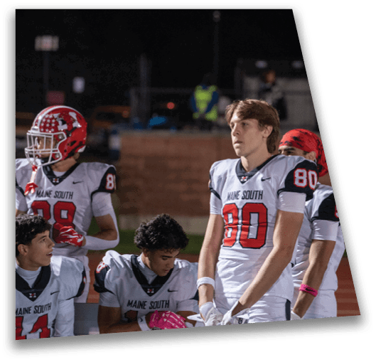 Three people in white football uniforms with red and black details stand on a field, with one person wearing a red bandana and another looking ahead with a focused expression. Description generated by AI