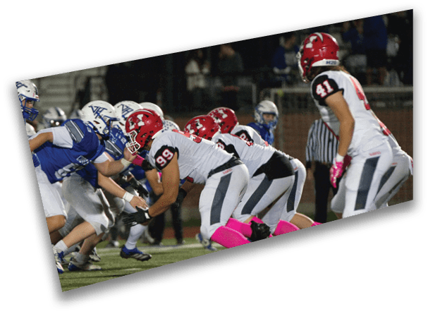 Two opposing football teams in blue and white and red and white uniforms are lined up facing each other on a field, ready for a play. Description generated by AI