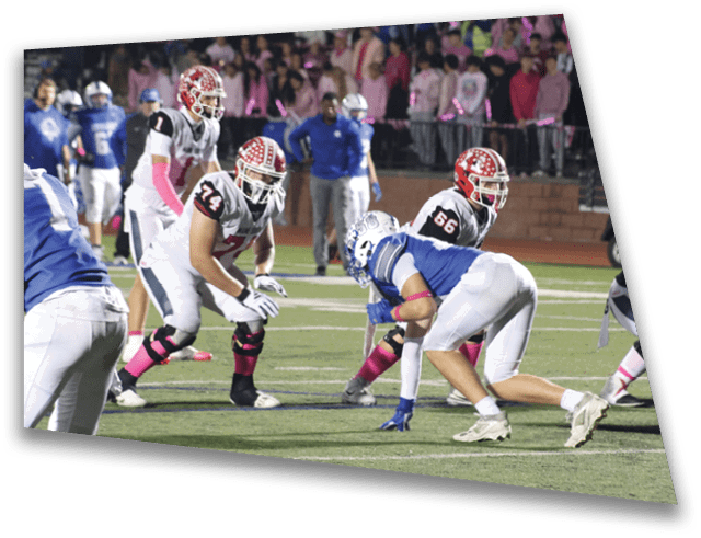 Players in football uniforms are positioned on a field preparing for a play with a crowd of spectators in the background. Description generated by AI