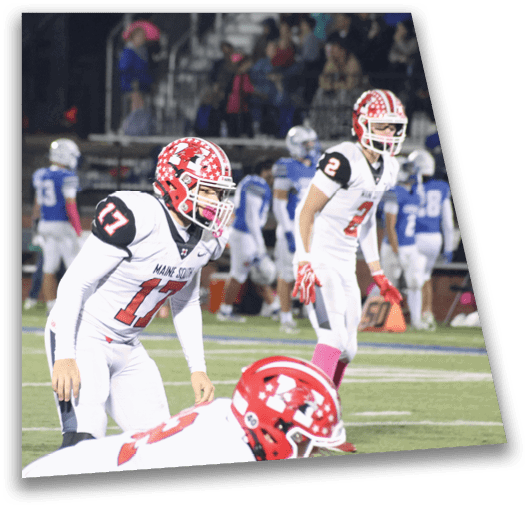 Three people in white football uniforms with red helmets are on a football field with other players and spectators in the background. Description generated by AI