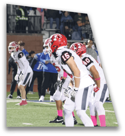 Several people in white and red football uniforms with helmets are lined up on a field, appearing ready for a play during a game. Description generated by AI
