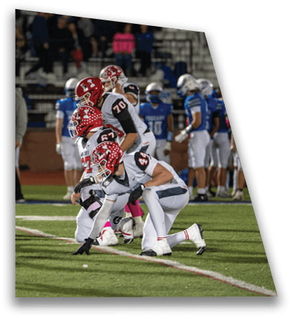 Several people in football uniforms are lined up on a field in a ready stance during a game with others and spectators in the background. Description generated by AI