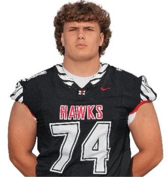 A person wearing a black sports jersey with the word “HAWKS" and the number 74 stands with one arm behind their back. Description generated by AI