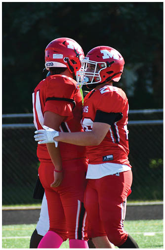 Three people wearing red football uniforms and helmets stand on a field with one person placing a hand on another's arm. Description generated by AI
