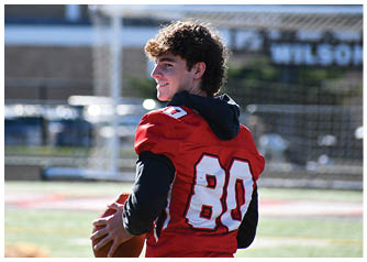 A person wearing a red football jersey with the number 80 is holding a football and looking to the side on a sports field. Description generated by AI
