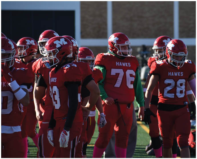 A group of people wearing red football uniforms and helmets are gathered on a field, with some standing and others appearing to be in conversation. Description generated by AI