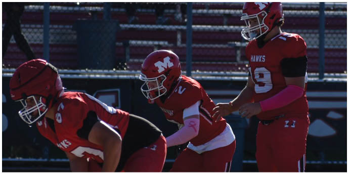 Three people in red football uniforms are positioned on a field, appearing to prepare for a play during a game. Description generated by AI