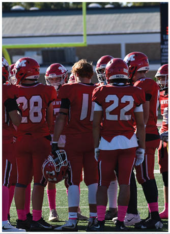 Four people wearing red football uniforms with helmets and pink socks are standing on a field, engaged in conversation. Description generated by AI