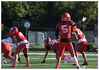 Several people wearing red and white football uniforms and helmets are positioned on a green field, preparing for a play during a game. Description generated by AI