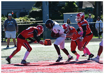 Children playing football on a field with one player in white running while three players in red attempt to tackle. Description generated by AI