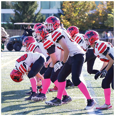 A group of people wearing football uniforms with red helmets and pink socks are lined up on a field facing opponents in green and gold uniforms. Description generated by AI