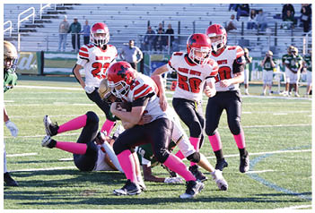 A group of people wearing football uniforms are engaged in a play on a grassy field with one person holding the ball tightly while others attempt to tackle or block. Description generated by AI