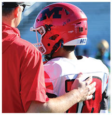 A person wearing a red football helmet and white jersey is being comforted by another person with a hand on their shoulder. Description generated by AI