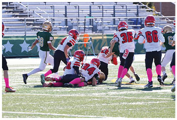 Several people wearing football uniforms are engaged in a play on a sunlit field, with some players on the ground and others standing nearby. Description generated by AI