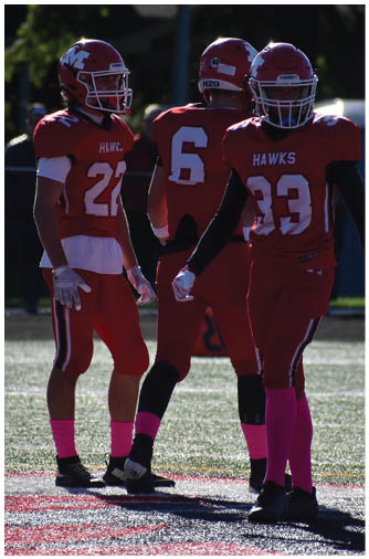 Two people wearing red football uniforms and helmets are standing close together, with one showing the number 6 on the back of their jersey. Description generated by AI
