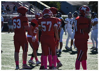 Several people wearing red football uniforms with pink socks are standing on a field while others in white uniforms are visible in the background. Description generated by AI