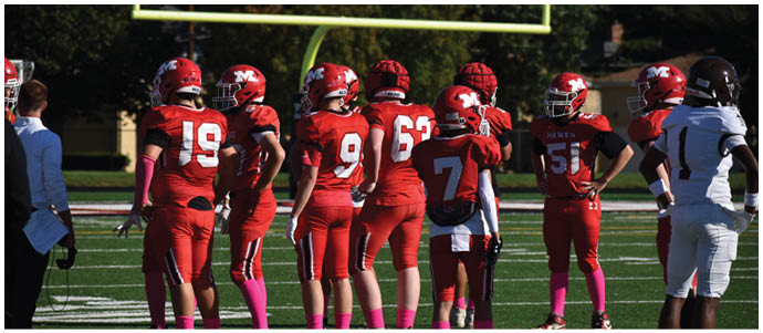 A group of people wearing red football uniforms and helmets stand on a football field with green turf and white yard lines. Description generated by AI