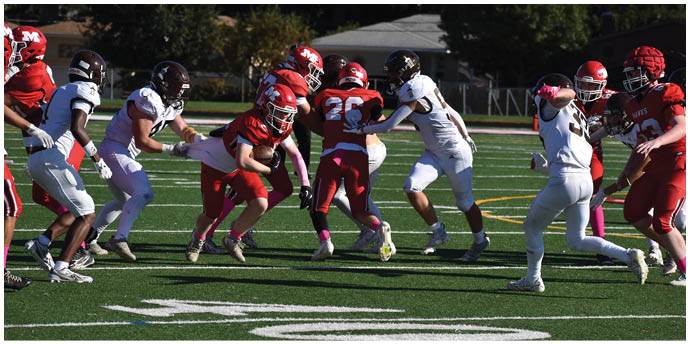 People wearing red and white football uniforms are engaged in a play on a green field with yard line markings. Description generated by AI